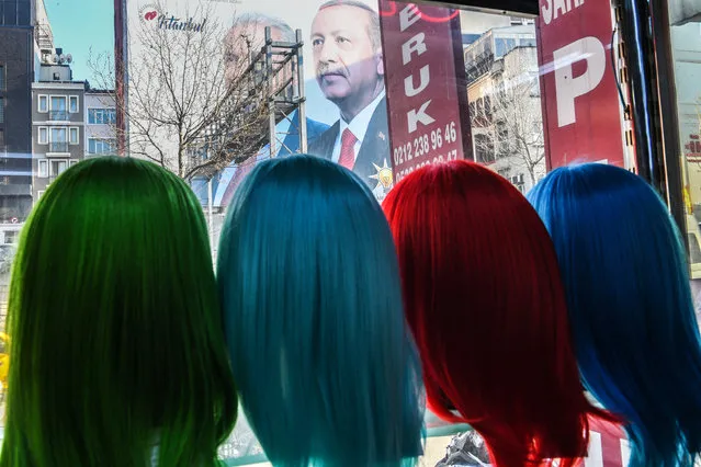 A giant election poster of the Turkish President covering the facade of a building is seen from a shop's window where wig models are displayed, in Istanbul on March 25, 2019, ahead of the March 31 local elections. (Photo by Ozan Kose/AFP Photo)