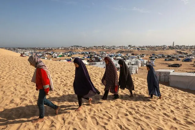 Palestinian girls walk on a sand dune toward a tent dedicated to Qoran reading, at a camp for displaced people in Rafah in the southern Gaza Strip on March 17, 2024, amid ongoing battles between Israel and the militant group Hamas. (Photo by Mohammed Abed/AFP Photo)