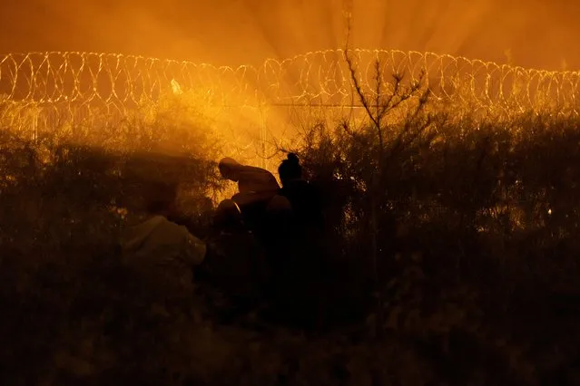 A man shears an opening through a razor wire-laden fence for a group of migrants from South and Central America as they prepare to enter into the United States from along the bank of the Rio Grande river, in El Paso, Texas on March 28, 2024. (Photo by Adrees Latif/Reuters)