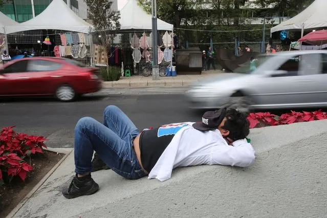 A migrant rests at Reforma Avenue during a gathering at the Anti Monument to the 72 migrants in Mexico City, Saturday, December 18, 2021, on International Migrants Day. In 2010, 72 migrants were assassinated in San Fernando, Tamaulipas. (Photo by Ginnette Riquelme/AP Photo)