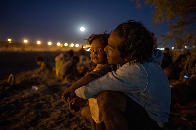 The Pink Moon rises in the background as Ismael Cruz, a 26-year-old migrant from Venezuela, caresses his one-year-old son Tobias Benjamin Cruz as they sit along the bank of the Rio Grande river while searching for an entry point into El Paso, Texas, from Ciudad Juarez, Mexico, on April 23, 2024. (Photo by Adrees Latif/Reuters)
