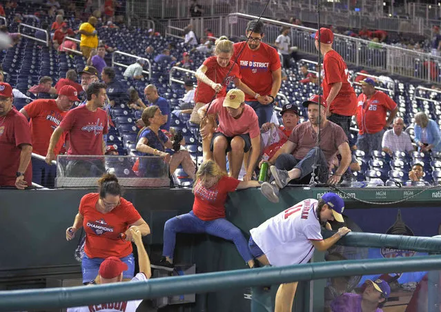 Fans jump into a camera well after hearing gunfire from outside the stadium, during a baseball game between the San Diego Padres and the Washington Nationals at Nationals Park in Washington on Saturday, July 17, 2021. (Photo by John McDonnell/The Washington Post via AP Photo)