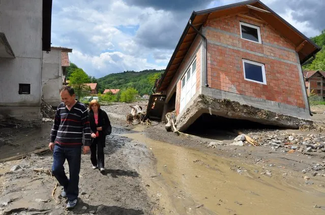 A picture made available 19 May 2014 shows people passing by damaged houses after flooding in Krupanj, 150 km southeast of Belgrade, Serbia, 18 May 2014. Clean-up began on 19 May after massive floods in parts of Serbia and Bosnia, even as cities on the river Sava braced for the arrival of a new wave of flooding. The situation was particularly grave in Krupanj, which has been without drinking water and electricity since 14 May, and Obrenovac, near Belgrade that saw the deaths of 12 people as flood waters covered most of the town. (Photo by Dragan Karadarevic/EPA)