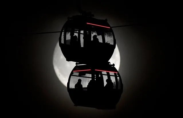 Passengers are seen silhouetted by the moon as they ride on the Emirates Air Line cable car over the River Thames in London, Britain, November 11, 2019. (Photo by Toby Melville/Reuters)