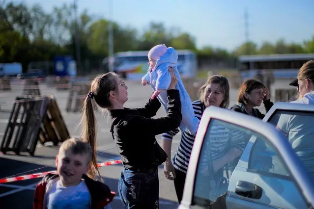 A woman holds up a baby as a family who fled from Enerhodar is reunited upon their arrival to a reception center for displaced people in Zaporizhzhia, Ukraine, Friday, May 6, 2022. Thousands of Ukrainian continue to leave Russian occupied areas. (Photo by Francisco Seco/AP Photo)