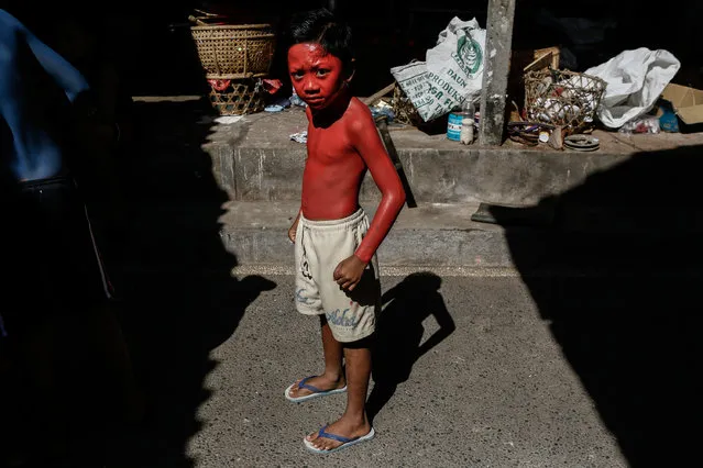 A boy dries the paint in the sun as he prepares for Grebeg Ritual on June 25, 2014 in Tegallalang Village, Gianyar, Bali, Indonesia. During the biannual ritual, young members of the community parade through the village with painted faces and bodies to ward off evil spirits. (Photo by Putu Sayoga/Getty Images)