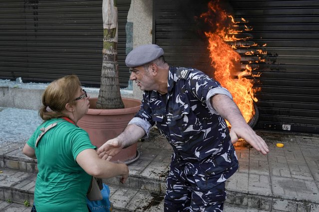 A police officer speaks with a protesting depositor as they stand in front of burning tires set on fire in front of a branch of Emirates Lebanese Bank in Dawra, a suburb north-east of Beirut, Thursday, August 29, 2024. Depositors for years have protested at the banks, demanding their trapped savings deposits, as they struggle from an economic crisis. (Photo by Bilal Hussein/AP Photo)