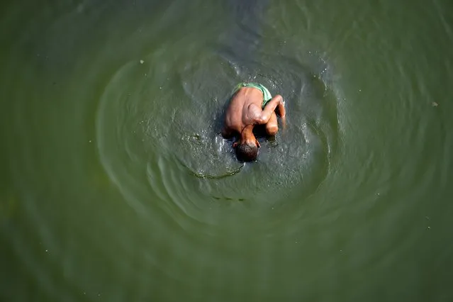 A boy searches for coins thrown by Hindu devotees in river Yamuna where water levels have reduced drastically following hot weather in New Delhi, India, Monday, May 2, 2022. The Indian capital, like many other parts of South Asia, is in the midst of a record-shattering heatwave. (Photo by Manish Swarup/AP Photo)