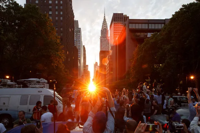 People watch Manhattanhenge, during which the setting sun aligns precisely with the east-west layout of the streets of Manhattan in New York, USA on July 11, 2016. (Photo by Xinhua/Barcroft Images)
