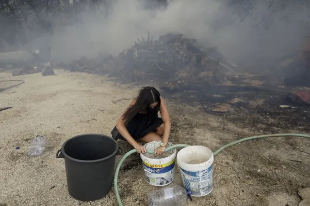 A young woman fills buckets with water for local residents trying to stop a forest fire from reaching their homes in the village of Figueiras, outside Leiria, central Portugal, Tuesday, July 12, 2022. Hundreds of firefighters in Portugal continue to battle fires in the center of the country that forced the evacuation of dozens of people from their homes mostly in villages around Santarem, Leiria and Pombal. (Photo by Joao Henriques/AP Photo)