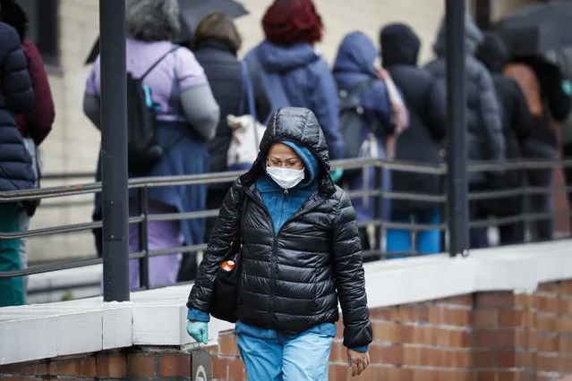A medical worker wearing a single protective glove and a face mask walks past a line of workers and visitors waiting to be tested for COVID-19, the disease caused by the new coronavirus, at the main entrance to the Department of Veterans Affairs Medical Center, Monday, March 23, 2020, in New York. (Photo by John Minchillo/AP Photo)