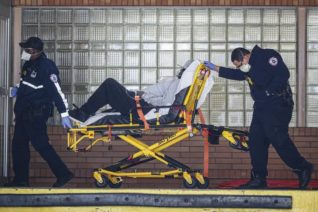 Paramedics wheel a patient wearing a breathing apparatus into the emergency room at Wyckoff Heights Medical Center, Monday, April 6, 2020, in New York. (Photo by John Minchillo/AP Photo)