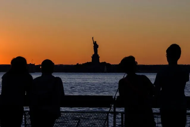 The Statue of Liberty is visible in the distance as people watch the sunset on August 12, 2022 in New York City. (Photo by Angela Weiss/AFP Photo)