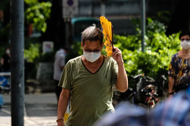 A man wears face mask and uses a fan to block the sun walks on a street on July 26, 2022 in Hong Kong, China. With the temperature reaching 35 degrees and above, the Very Hot Weather persist 13 days in a row and will continue till the end of July. (Photo by Keith Tsuji/Rex Features/Shutterstock)