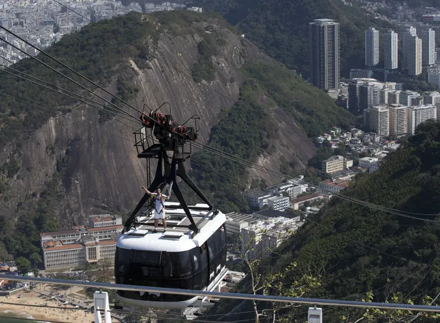 Sugar Loaf worker Diego Scofano carries the Olympic torch while standing on top of a moving cable car toward the tourist attraction Sugar Loaf mountain on its way to the Rio's 2016 Summer Olympics  opening ceremony venue, in Rio de Janeiro, Brazil, Friday, August 5, 2016. (Photo by Silvia Izquierdo/AP Photo)
