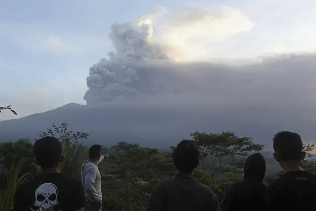 Villagers watch the Mount Agung volcano erupting during sunrise in Karangasem, Bali island, Indonesia, Sunday, November 26, 2017. A volcano on the Indonesian tourist island of Bali erupted for the second time in a week on Saturday, disrupting international flights even as authorities said the island remains safe. (Photo by Firdia Lisnawati/AP Photo)