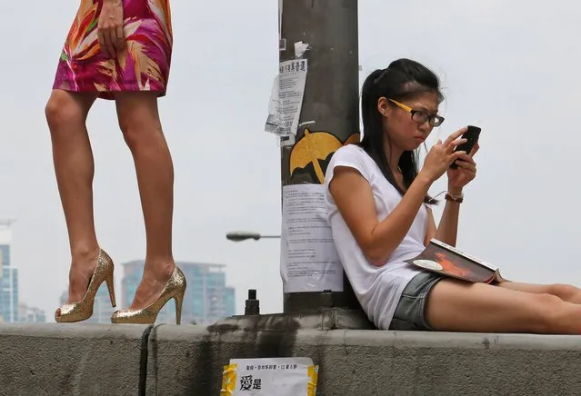 A model, left, poses for a fashion photo shooting as a protester sits on a main road in the occupied areas outside government headquarters in Hong Kong's Admiralty, Friday, October 10, 2014. A pro-democracy protest that has blocked main roads in Hong Kong for almost two weeks could drag on for days yet, after talks aimed at resolving a bitter standoff between the city's government and student demonstrators collapsed Thursday. (Photo by Kin Cheung/AP Photo)