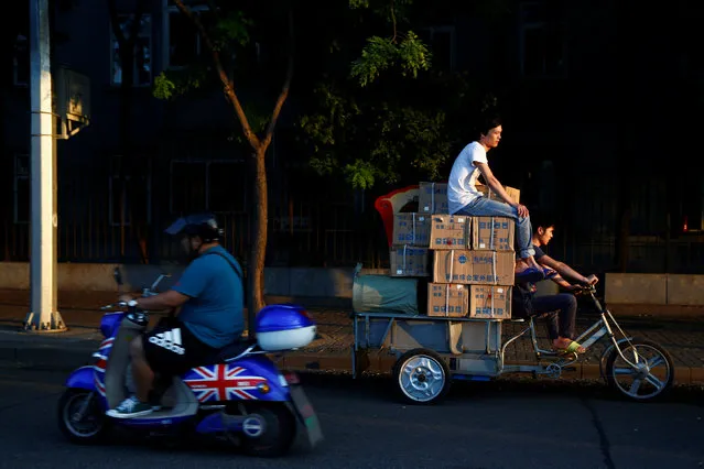 A man sits on top of boxes on a delivery tricycle as a man rides past on a scooter sporting the British flag in central Beijing, China, August 19, 2016. (Photo by Thomas Peter/Reuters)