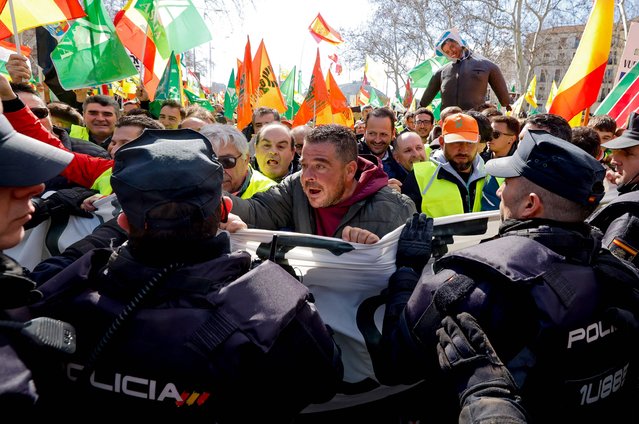 Farmers face police officers during a protest to denounce their conditions and the European agricultural policy, in Madrid, on February 26, 2024. Spanish farmers and livestock breeders demanding product prices to cover their production costs, and for non-EU imports to face the same regulations they do, resume protest as EU agriculture ministers meet in Brussels on February 26, 2024. Spanish farmers are part of a wider movement that has seen roads blocked in France, Germany, Italy, Poland and Greece, among other countries. (Photo by Oscar Del Pozo/AFP Photo)