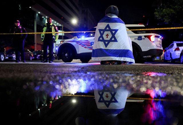 A man, with an Israeli flag with a cross in the center, kneels next to emergency personnel working at the site where, according to the U.S. Homeland Security Secretary, two Israeli embassy staff were shot dead near the Capital Jewish Museum in Washington, on May 22, 2025. (Photo by Jonathan Ernst/Reuters)