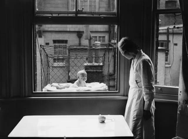 A nanny supervising a baby suspended in a wire cage attached to the outside of a high tenement block window in United Kingdom, 23rd June 1937. The cages are distributed to members of the Chelsea Baby Club who have no gardens and live at the top of high buildings. (Photo by Reg Speller/Fox Photos/Getty Images)