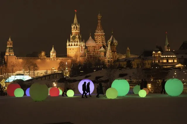 People walk at Zaryadye Park decorated for the New Year and Christmas festivities with the Kremlin Wall, the Spasskaya Tower, and the St. Basil's Cathedral in the background in Moscow, Russia, Thursday, December 29, 2022. (Photo by Alexander Zemlianichenko/AP Photo)