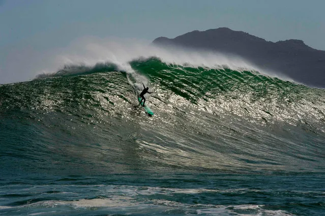 A surfer catches a wave at Sunset, a surfing spot between Hout Bay and Kommetjie that produces some of South Africa's biggest waves, in Cape Town on September 19, 2020. This spot needs a variety of conditions to come together, like wind, swell size, wave period and direction, that often follows storms, to produce huge waves on this reef, which attracts and challenges the surfers. (Photo by Rodger Bosch/AFP Photo)