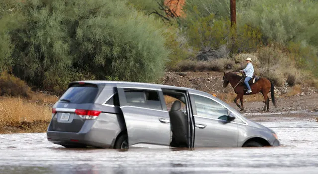 A horseback rider takes a look at a car as it rests abandoned in the floodwaters of Skunk Creek after the driver was rescued Tuesday, October 20, 2015, in Desert Hills, Ariz. Heavy rains swept through many areas of Arizona, like Desert Hills just north of the Phoenix metro area. (Photo by Ross D. Franklin/AP Photo)