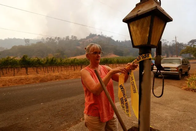 Cindi Frediani ties yellow tape on a post, to let officials know they have been told to leave, as smoke from fire is seen coming over the hillside across the valley, in Calistoga, California, September 28, 2020. (Photo by Fred Greaves/Reuters)
