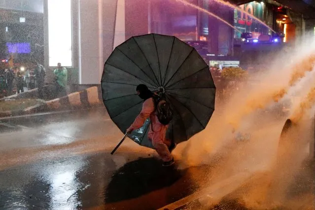 A man takes cover behind an umbrella during an anti-government protest, in Bangkok, Thailand on October 16, 2020. (Photo by Jorge Silva/Reuters)