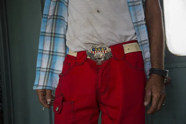 In this March 23, 2015 photo, a cowboy wearing a U.S.A. belt buckle smokes on the landing of a train car as he travels to a rodeo  in the province of Holguin, Cuba. From east to the west, trains offer a fine-grained, slow-moving view of Cuba that few foreigners ever see. (Photo by Ramon Espinosa/AP Photo)