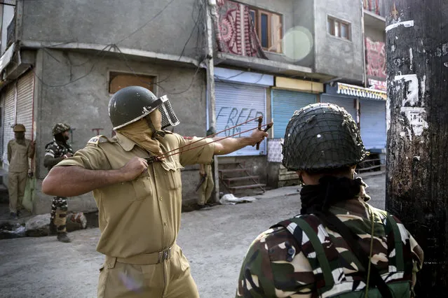 An Indian policeman uses a sling to shoot glass marbles at Kashmiri protesters during a protest in Srinagar, Indian controlled Kashmir, Friday, October 7, 2016. (Photo by Dar Yasin/AP Photo)
