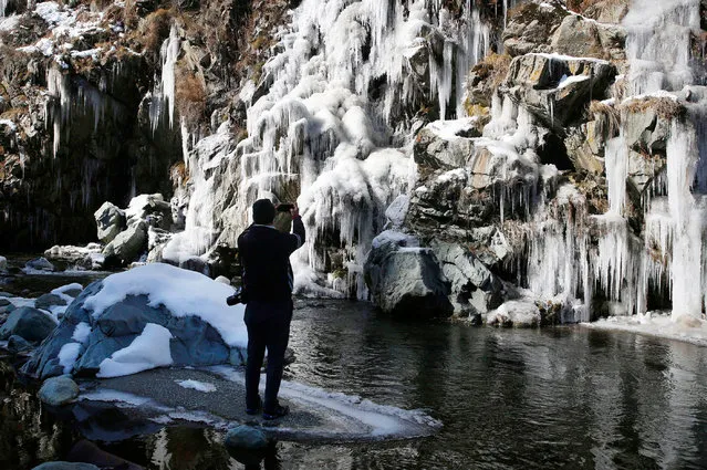 A Kashmiri man takes a photograph of a partially frozen waterfall in Tangmarg area of northern Kashmir, 16 December 2020. Srinagar records the season's lowest temperatures at minus 4.8 degrees Celsius while Drass town in Ladakh remained frozen at minus 18.6 degrees, according to local news reports. (Photo by Farooq Khan/EPA/EFE)