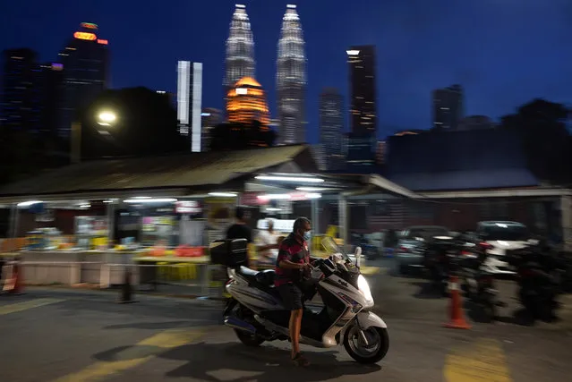 A motorcyclist wears a face mask with the background of Twin Towers in downtown Kuala Lumpur, Malaysia, Monday, January 11, 2021. Prime Minister Muhyiddin Yassin says Malaysia's health care system is at a breaking point as he announced new movement curbs, including near-lockdown in Kuala Lumpur and several high-risk states to rein in a spike in coronavirus cases. (Photo by Vincent Thian/AP Photo)