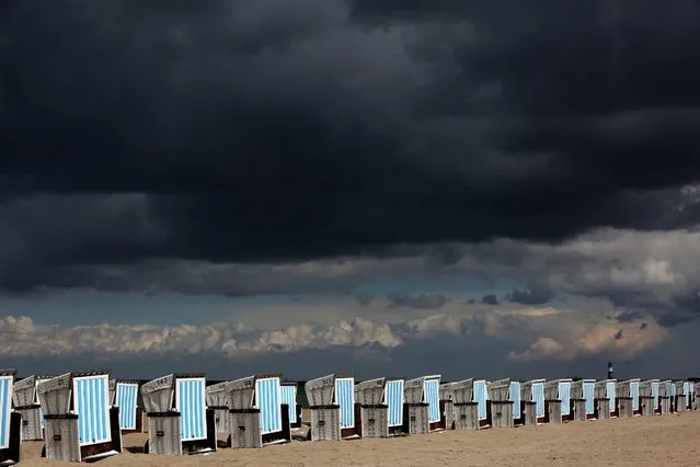 Dark clouds move over canopied beach chairs standing in the sun in Rostock-Warnemuende, Germany, 25 April 2016. A mixture of rain, snow, and showers of sleet with sun in-between makes for classic April weather. (Photo by Bernd Wuestneck/EPA)
