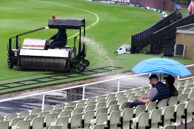 A member of ground staff clears water from the field as fans sit in the stands with umbrellas, as rain delays the start of England v Australia play at Edgbaston Cricket Ground in Birmingham, Britain on June 20, 2023. (Photo by Paul Childs/Action Images via Reuters)