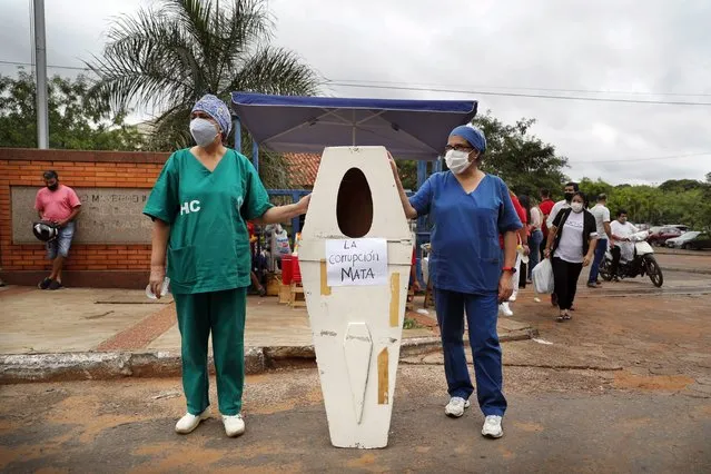 Nurses who work at the Hospital de Clinicas hold up an empty coffin with the Spanish message “Corruption kills” before the start of a protest demanding more medical supplies outside their public hospital in San Lorenzo, Paraguay, Thursday, March 4, 2021, amid the COVID-19 pandemic. Paraguay has canceled non-emergency surgeries in all public hospitals due to a flood of COVID-19 patients that has overwhelmed intensive care units. (Photo by Jorge Saenz/AP Photo)