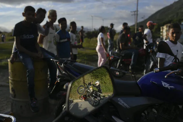 Reflected in a motorcycle side mirror, stuntman Pedro Aldana performs a wheelie on his motorbike during an exhibition in the Ojo de Agua neighborhood of Caracas, Venezuela, Sunday, January 10, 2021. “This is my passion and my work”, he said. (Photo by Matias Delacroix/AP Photo)