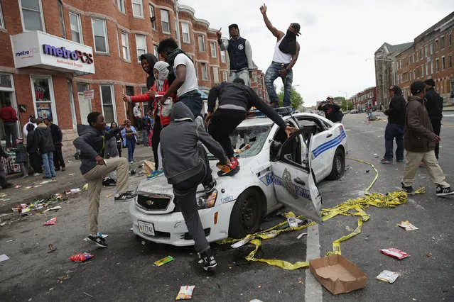 Demonstrators climb on a destroyed Baltimore Police car in the street near the corner of Pennsylvania and North avenues during violent protests following the funeral of Freddie Gray April 27, 2015 in Baltimore, Maryland. Gray, 25, who was arrested for possessing a switch blade knife April 12 outside the Gilmor Homes housing project on Baltimore's west side. According to his attorney, Gray died a week later in the hospital from a severe spinal cord injury he received while in police custody. (Photo by Chip Somodevilla/Getty Images)