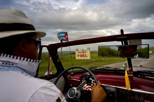 In this July 24, 2018 photo, a taxi driver steers his classic American car past a sign that says in Spanish вЂњI'm FidelвЂќ on the road to Guantanamo, Cuba, near the U.S. Guantanamo Bay naval base. People on both sides of the closely monitored boundary have long led different lives, yet they all live under government restrictions and appeals to patriotism. (Photo by Ramon Espinosa/AP Photo)