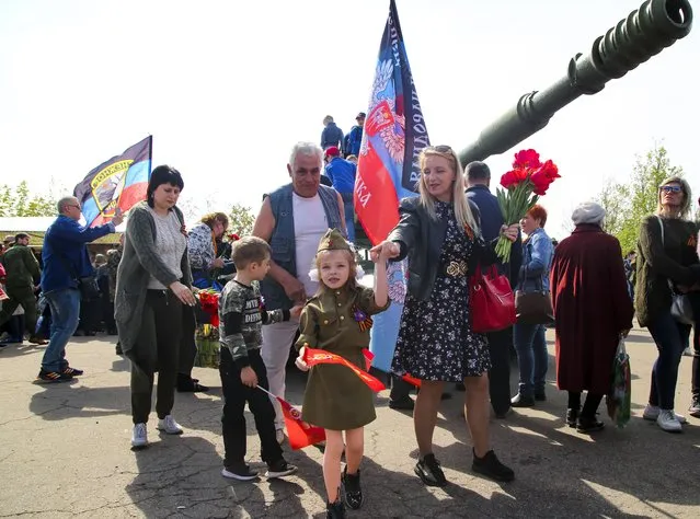 A girl wearing Soviet-era military uniform and her relative walks past a cannon during celebrations of the Victory Day at a World War II memorial in Saur-Mogila, about 60 km (31 miles) east of Donetsk, eastern Ukraine, Saturday, May 8, 2021. Efforts have stalled to end the conflict between Russia-backed rebels and Ukrainian forces, which has killed more than 14,000 people since it broke out in 2014. Russia, which claims it has no military presence in eastern Ukraine, fueled the tensions this year by massing troops and conducting large-scale military exercises near its border with Ukraine. (Photo by Alexei Alexandrov/AP Photo)