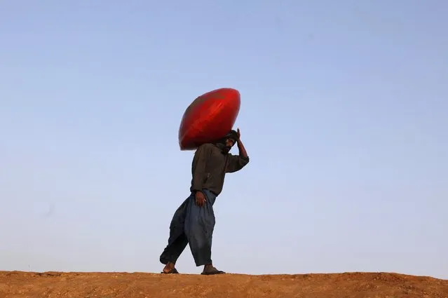 A man carries a floating pitcher which he uses to catch fish while heading home in Soneri village next to Keenjhar Lake, near Thatta, February 22, 2015. (Photo by Akhtar Soomro/Reuters)