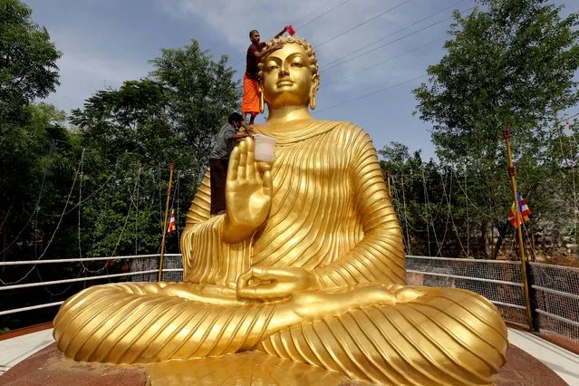 A Buddhist monk climbs atop a giant statue of Buddha, to wash and decorate on the eve of Buddha Purnima, a holiday traditionally celebrated for Buddha's birthday also known as Vesak celebrations, in Bhopal on May 25, 2021. (Photo by Gagan Nayar/AFP Photo)