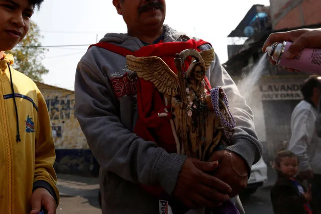 A man carries a figurine of Santa Muerte or The Saint of Death as it sprayed as a symbol of offering during the first prayer of the New Year in Mexico City, Mexico January 1, 2017. (Photo by Carlos Jasso/Reuters)