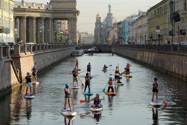 People steer their SUP-Boards in central St. Petersburg, Russia, early Thursday, July 15, 2021. People are permitted to use rowing boats and SUP boards on the rivers and canals of St. Petersburg in the early mornng when floating on motorboats are prohibtied. (Photo by Dmitri Lovetsky/AP Photo)