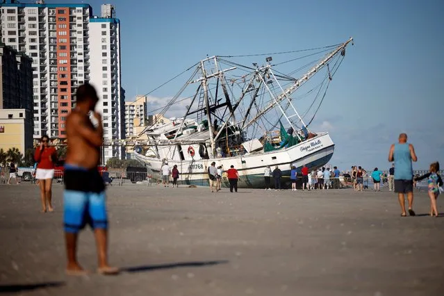 Beachgoers look at a large shrimping boat that was swept ashore by hurricane Ian in Myrtle Beach, South Carolina, U.S., October 1, 2022. (Photo by Jonathan Drake/Reuters)