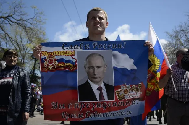 A man carries a poster showing a portrait of  Russian President Vladimir Putin and reading “Glory to Russia! We are with the president! Crimea and Sevastopol”,  during celebrations marking the 70th anniversary of the victory over Nazi Germany in WWII in Sevastopol, Crimea, Saturday, May 9, 2015. (Photo by Anton Volk/AP Photo)
