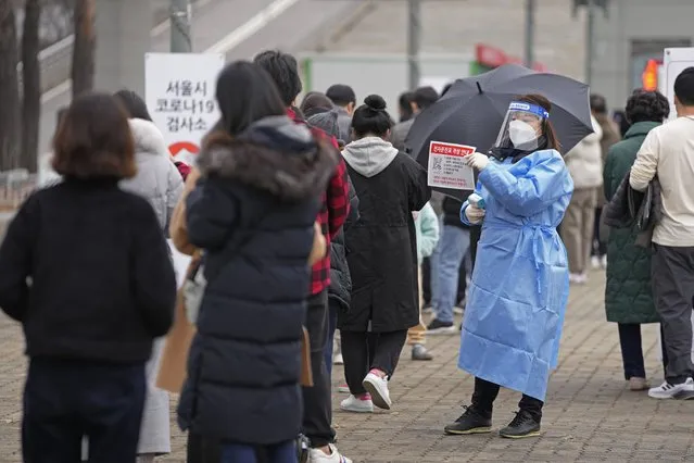 A medical worker holds a sign for visitors to prepare for the coronavirus tests at a temporary screening clinic for coronavirus in Seoul, South Korea, Friday, December 10, 2021. New coronavirus infections in South Korea exceeded 7,000 for the third consecutive day on Friday in a record-breaking surge that has crushed hospitals and threatens the country's goals to weather the pandemic without lockdowns. (Photo by Lee Jin-man/AP Photo)