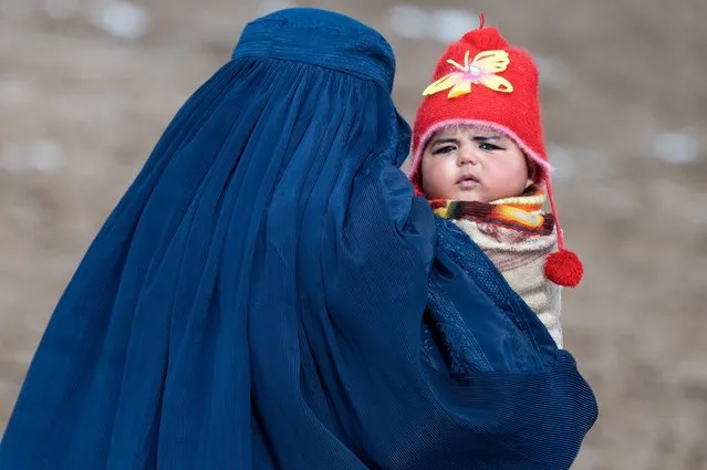 This photograph taken on February 25, 2024 shows an Afghan burqa-clad woman carrying a child to a health post to inoculate him during the “outreach vaccination” program, a routine immunization work in the Aab Bareek village of Argo district at the Badakhshan province. (Photo by Wakil Kohsar/AFP Photo)