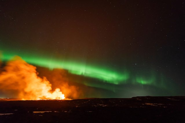 View of the eruption area with the northern lights dancing in the sky near the town of Grindavik, Iceland, Thursday, March 28, 2024. The volcano in southwestern Iceland that erupted three times in December, January and February, sending lava towards a nearby community, keeps erupting. (Photo by Marco di Marco/AP Photo)